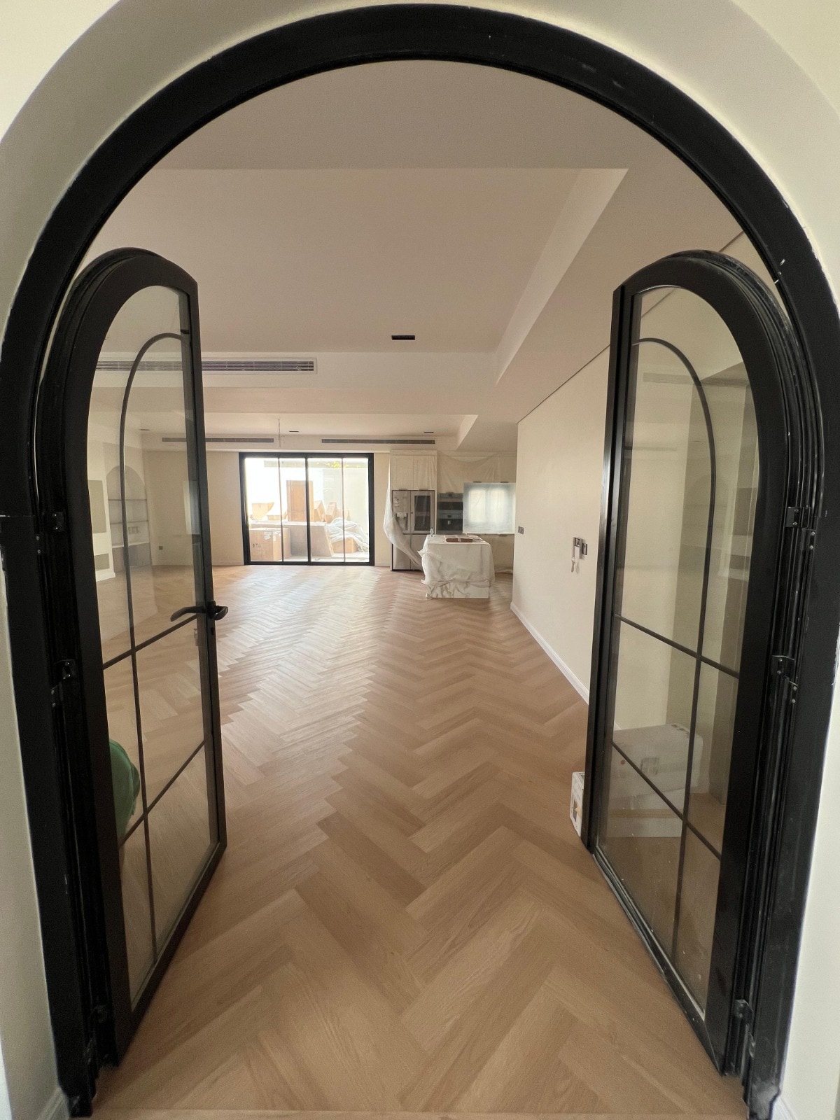 Pale herringbone oak continuing beyond a pair of black arched doors